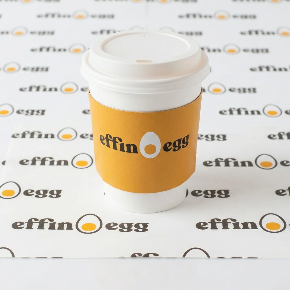 White Effin' Egg coffee cup with an orange sleeve, on a white background with the brand logo.