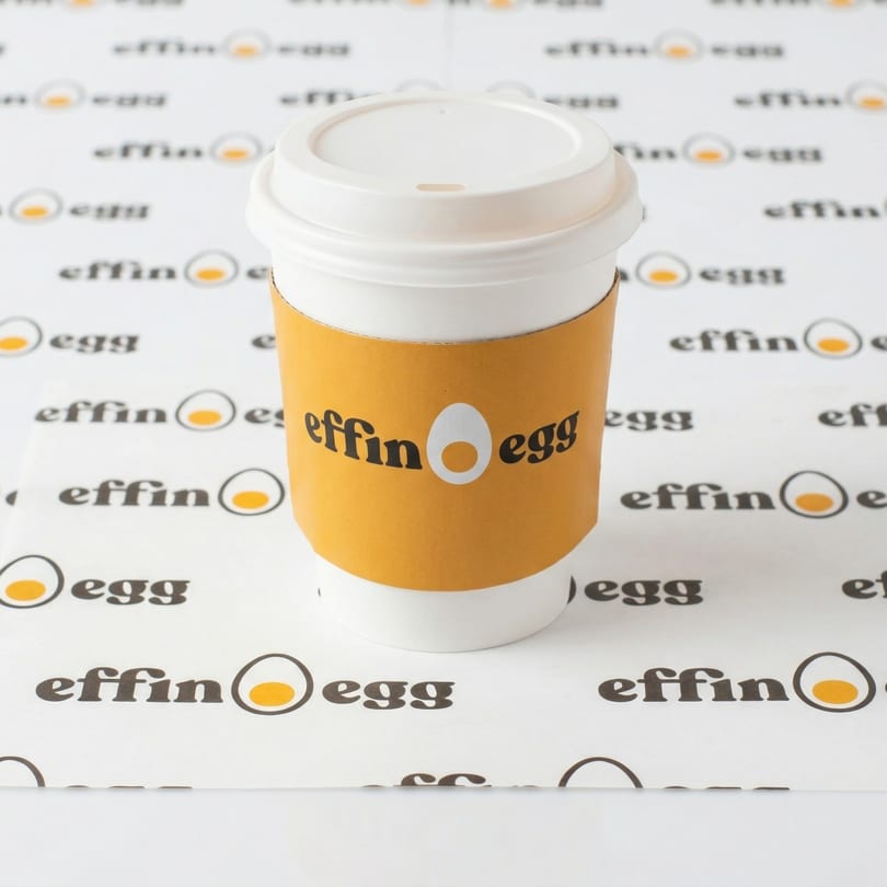 White Effin' Egg coffee cup with an orange sleeve, on a white background with the brand logo.