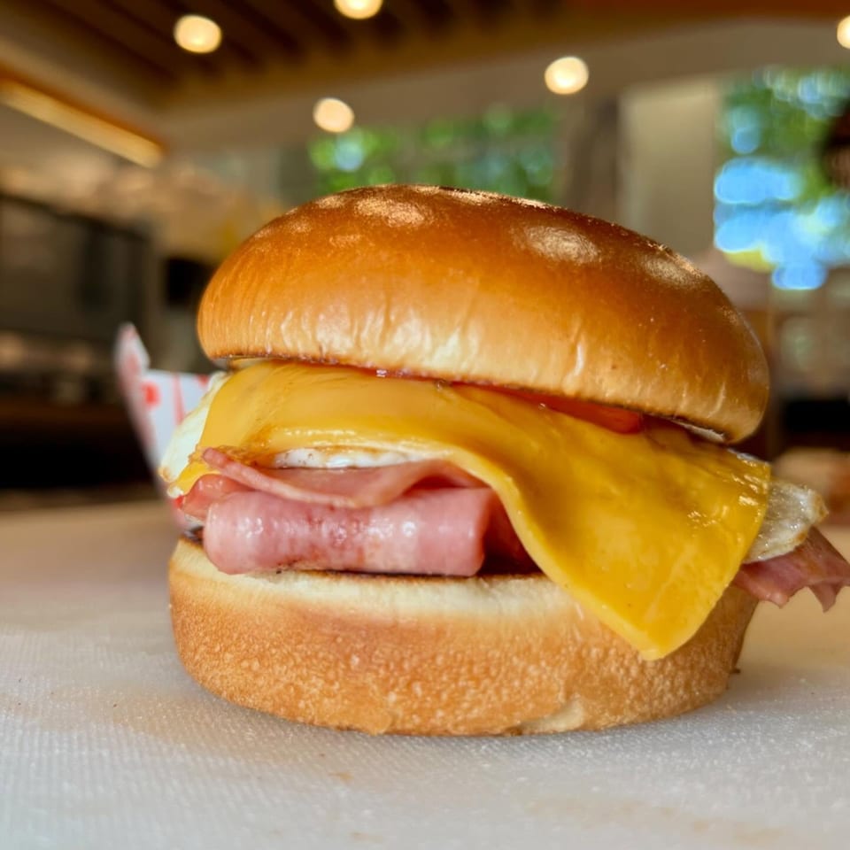 A breakfast sandwich with ham, egg, and cheese on a toasted bun, on a white surface.