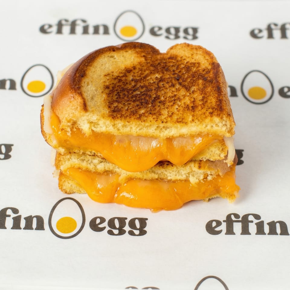 Grilled cheese sandwich with melted orange cheese on toasted bread, on an Effin Egg branded paper.