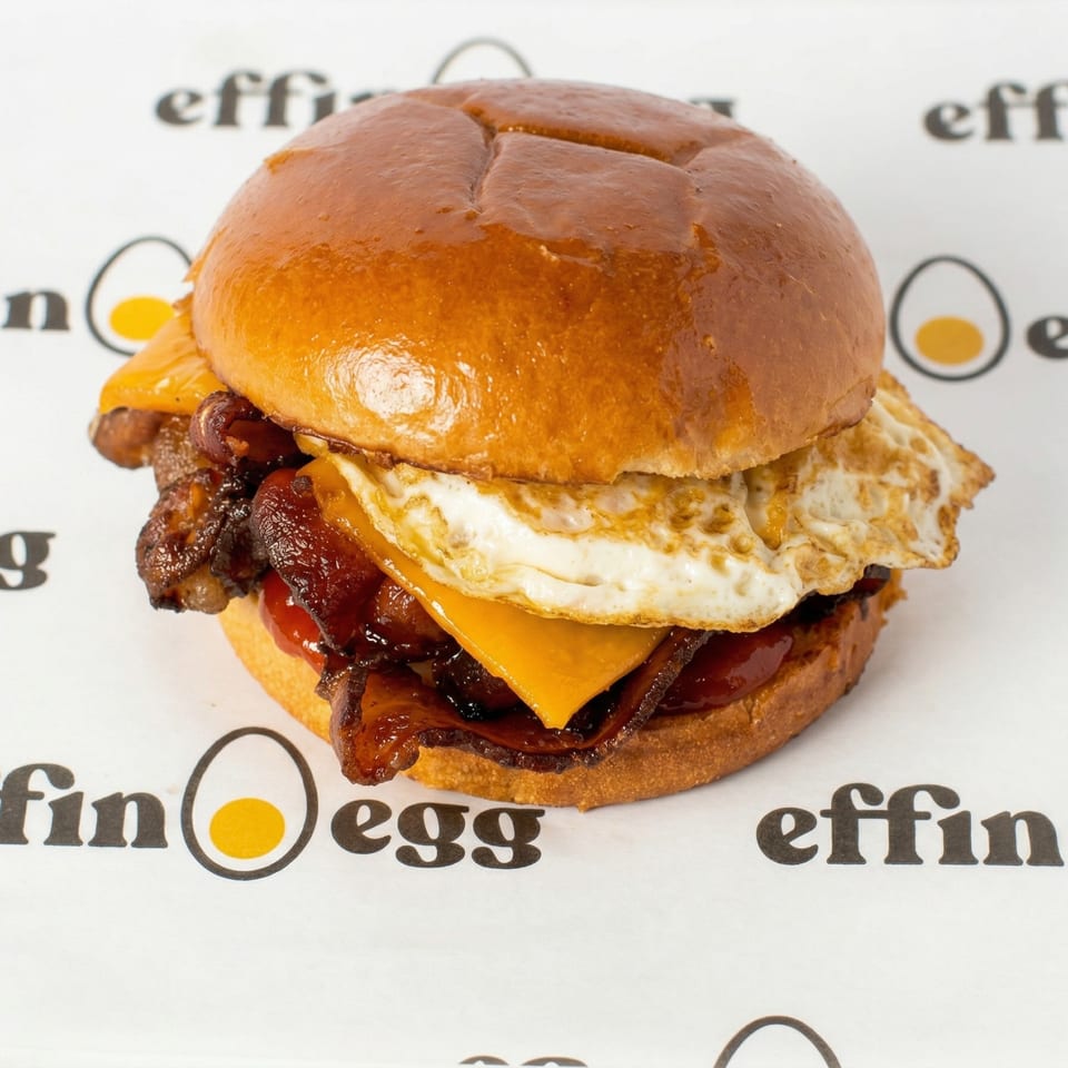 A close-up of an Effin Egg breakfast sandwich with bacon, egg, and cheese on a brioche bun.